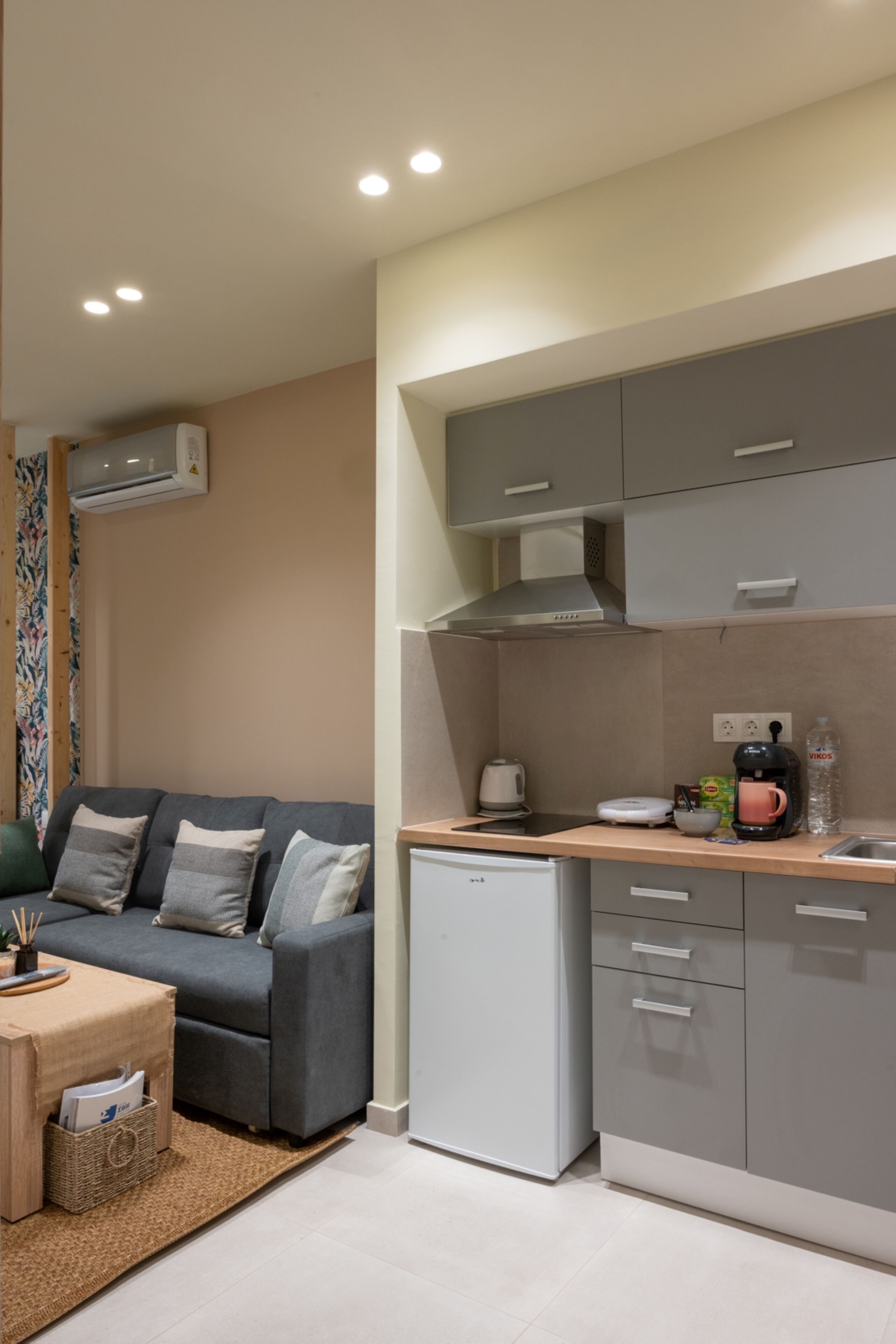 A compact kitchen with grey cabinets, a small fridge, and a wooden countertop.