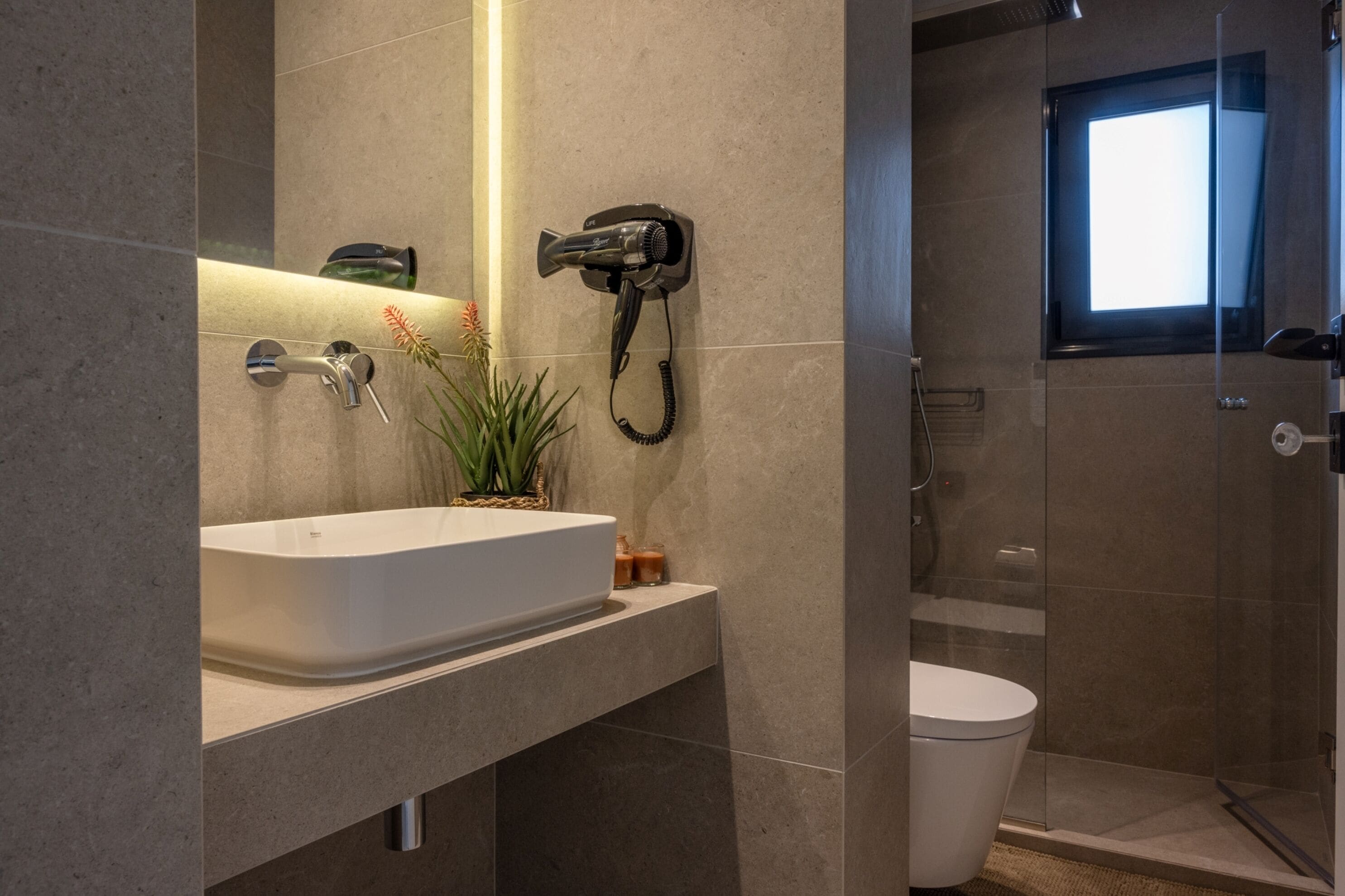 Ein modernes Badezimmer mit einem weißen Waschbecken, einem an der Wand montierten Fön und einer Duschkabine aus Glas.