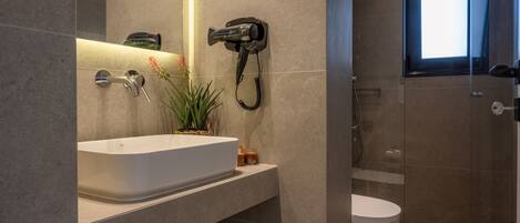 A modern bathroom with a white sink, a hairdryer mounted on the wall, and a glass-enclosed shower area.