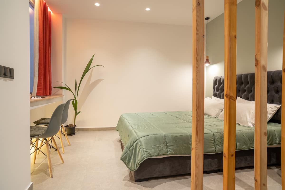 A bedroom with a bed, a desk, chairs, and a potted plant.