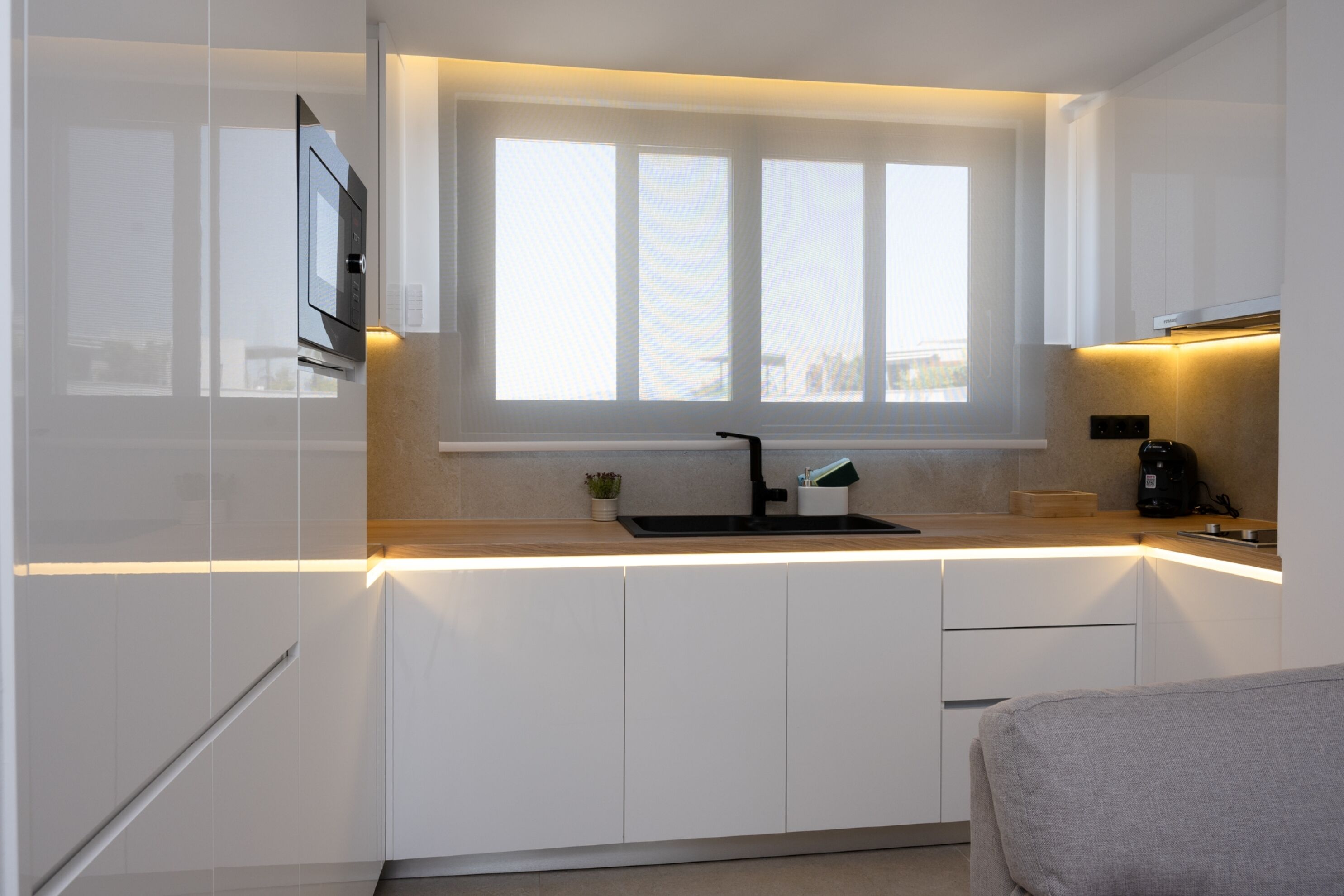 A modern kitchen with white cabinets, a black sink, a window above the counter, and a coffee maker on the countertop.