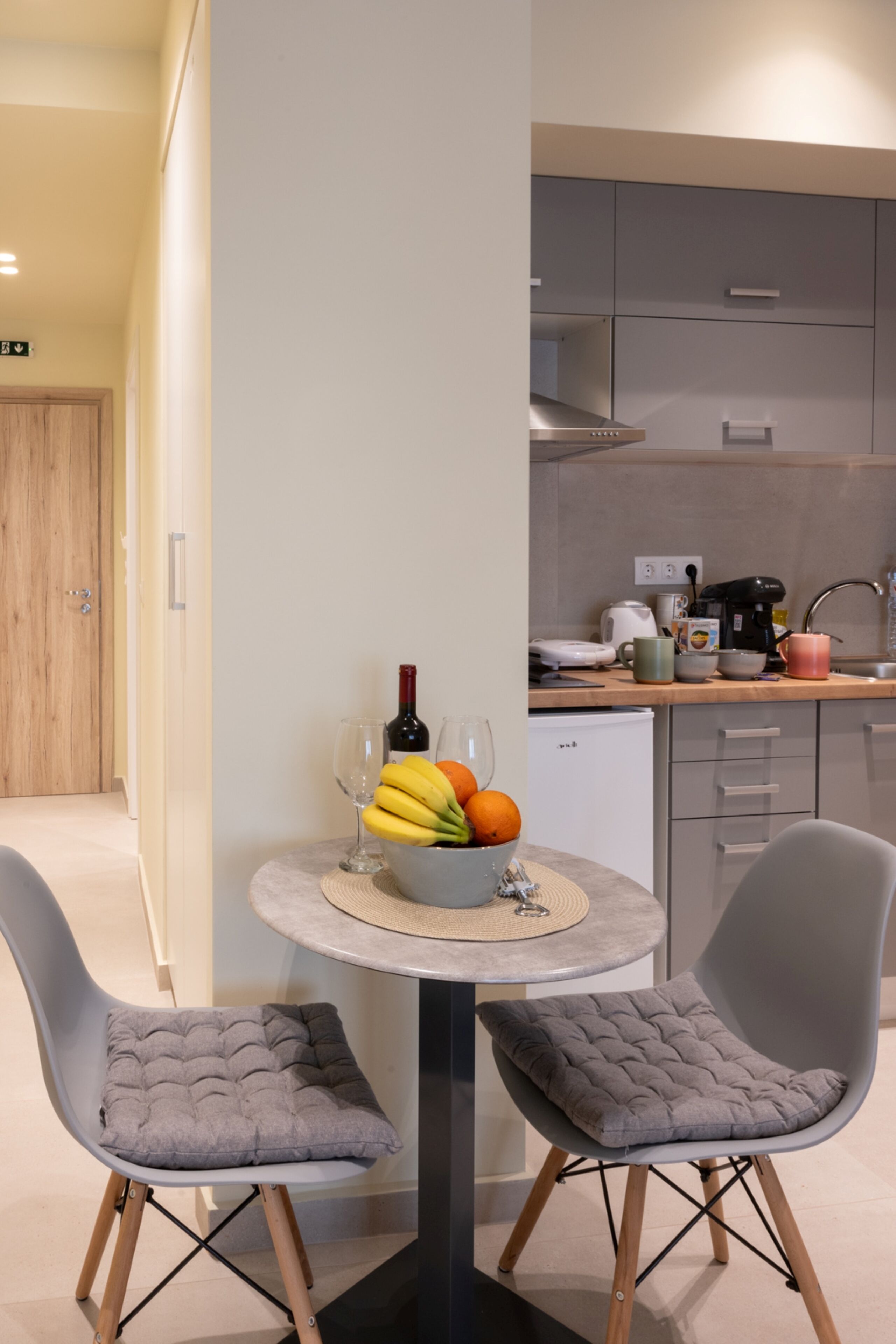 A modern kitchen with grey cabinets, a small fridge, and a dining area with two grey chairs and a table.
