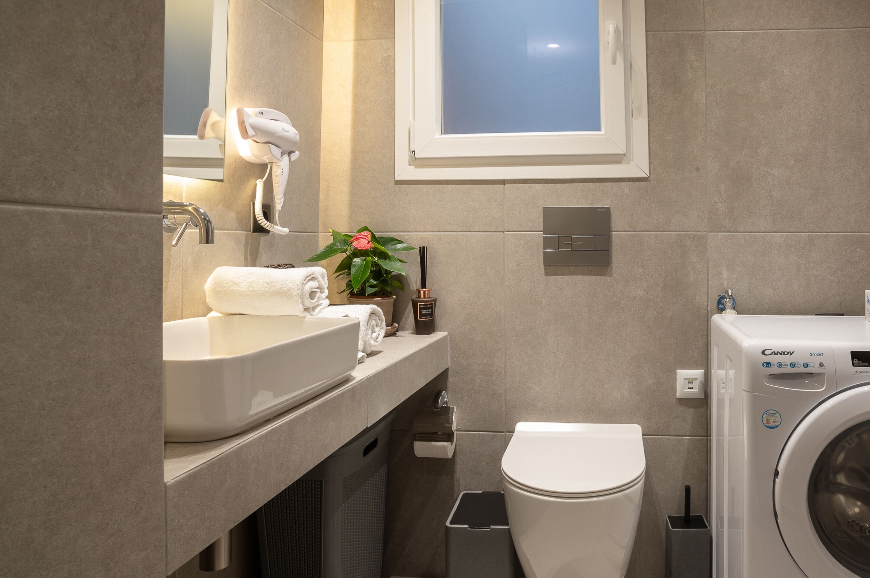 A modern bathroom with a sink, mirror, towel, toilet, and a washing machine.