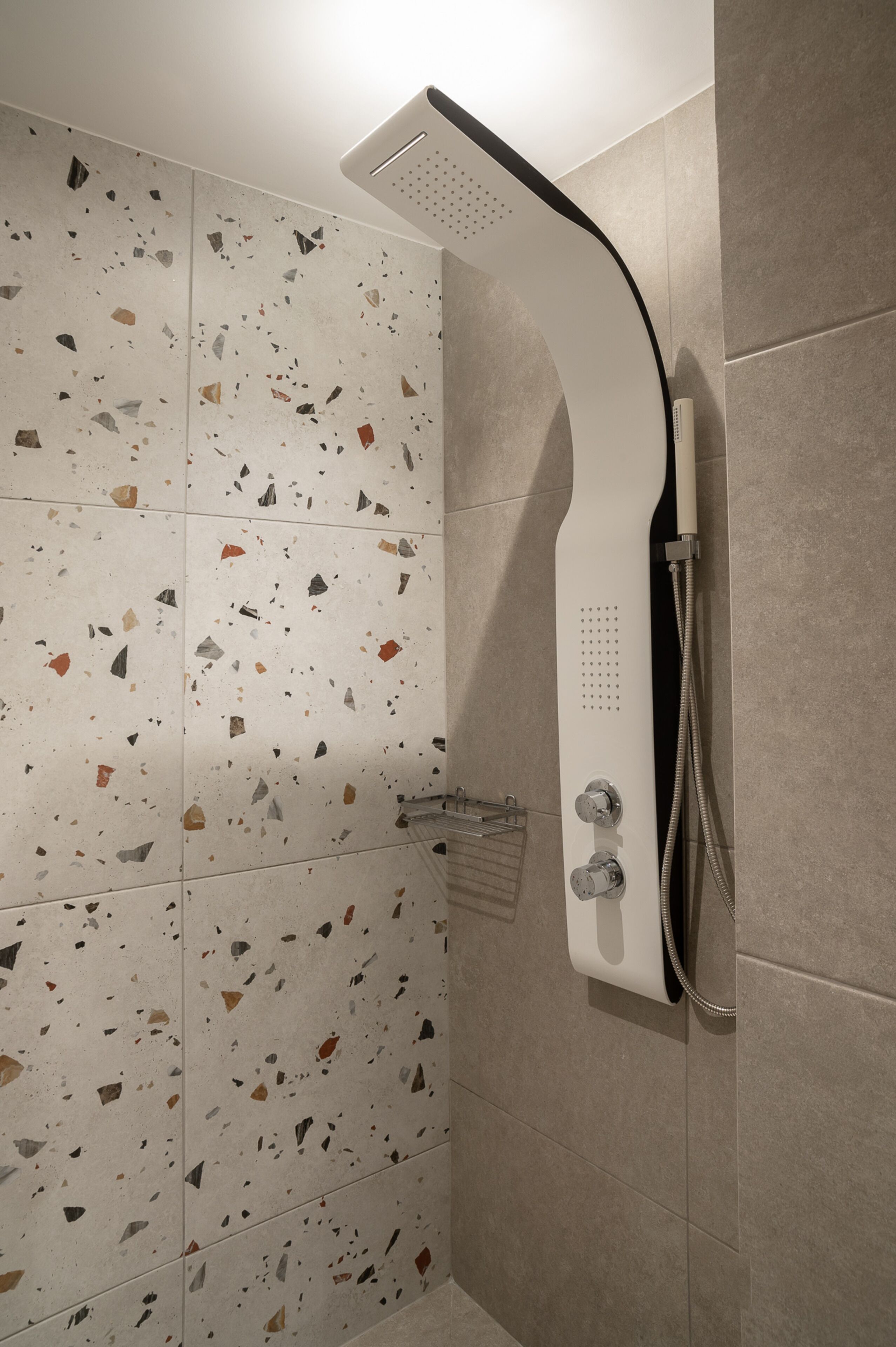 A shower with a curved head and a handheld showerhead, mounted on a wall with terrazzo tiles.