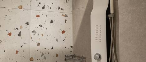 A shower with a curved head and a handheld showerhead, mounted on a wall with terrazzo tiles.