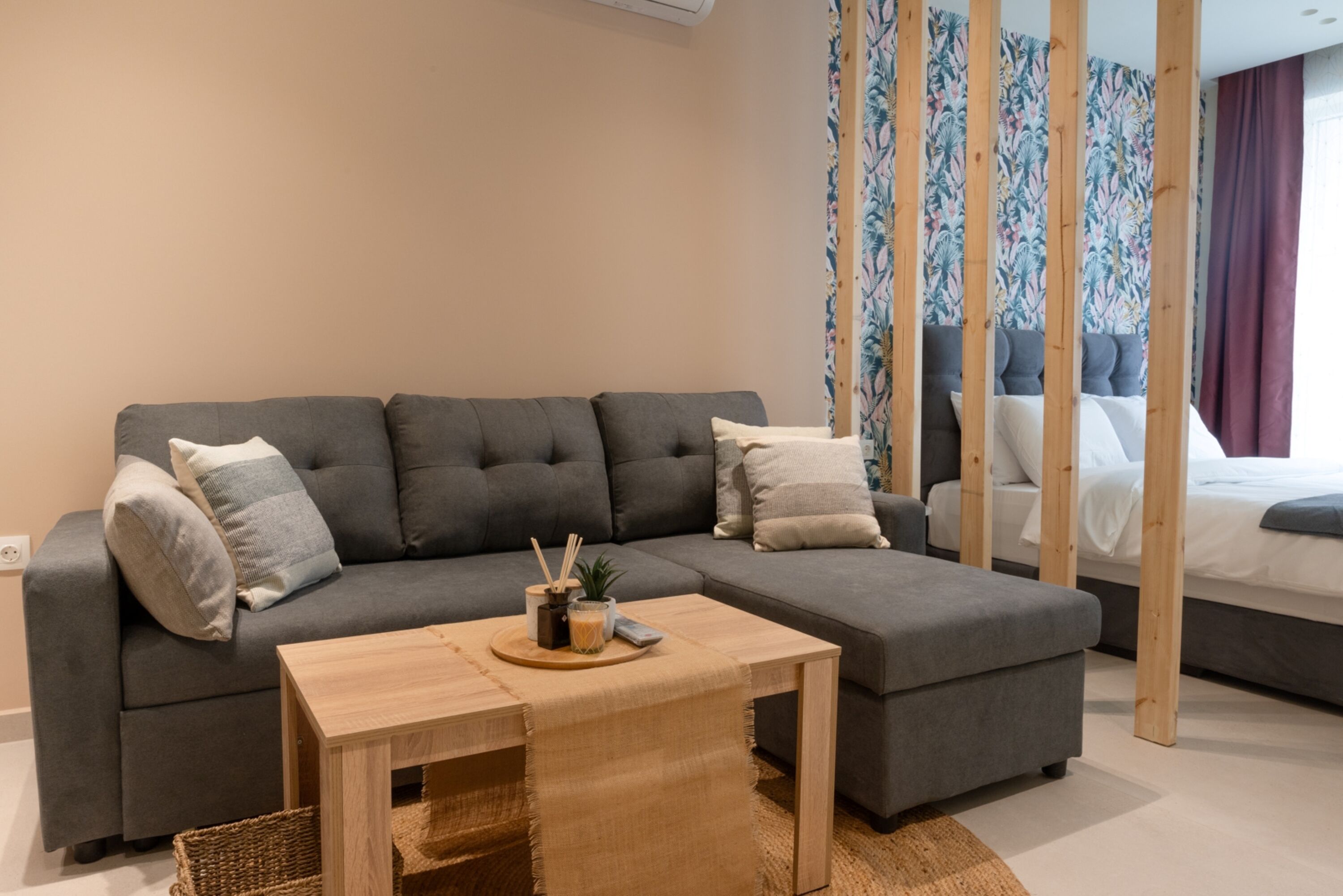 Een moderne woonkamer met een grijze modulaire bank, een houten salontafel en een bed met hoofdeinde.