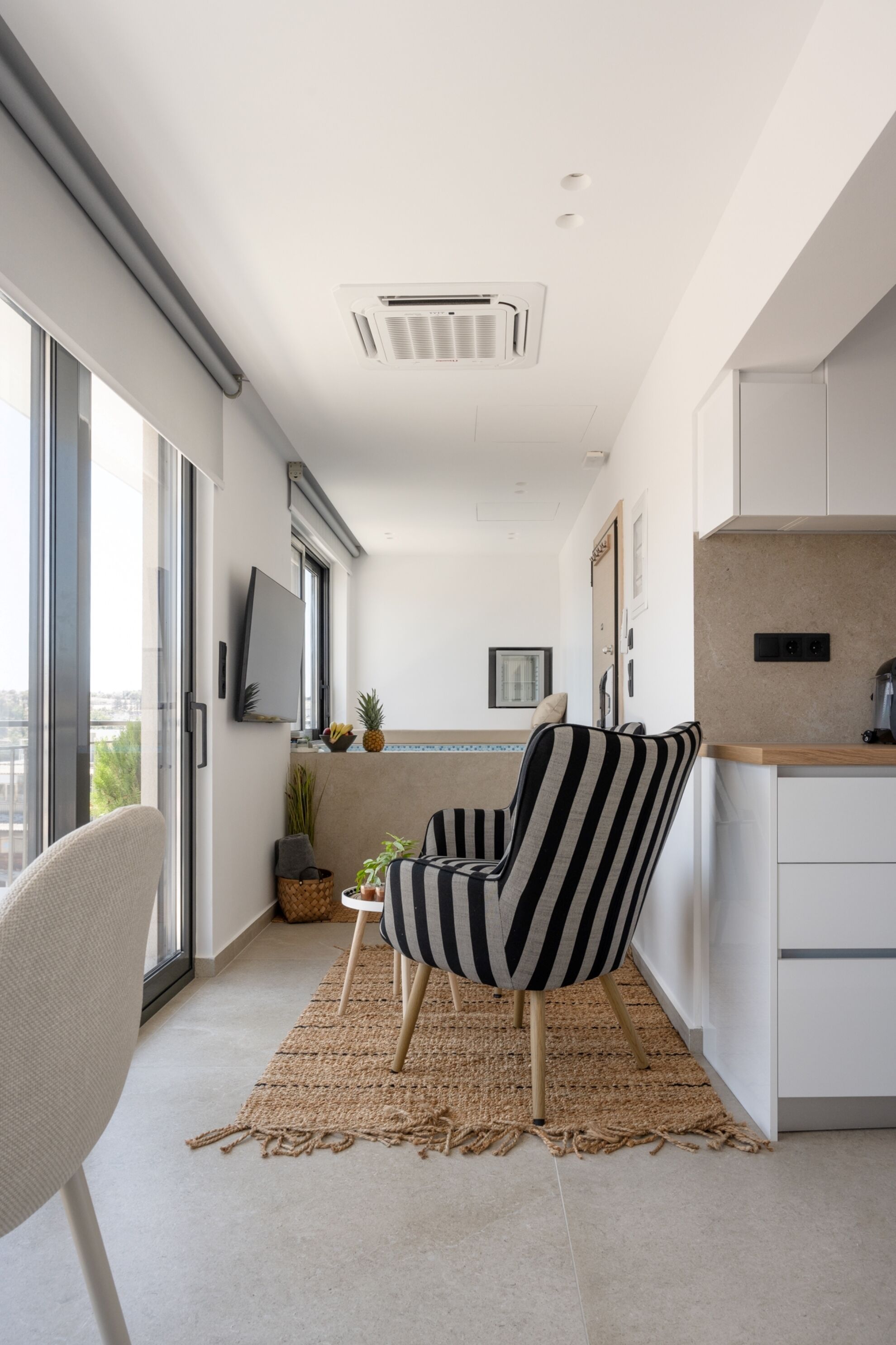 A modern kitchen with a large window, a striped chair, and a flat-screen TV.