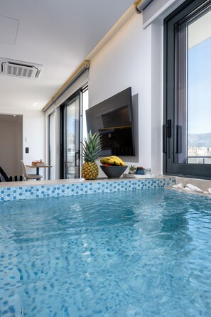 A modern indoor pool with clear blue water, a pineapple, and a bowl of fruit on the edge.