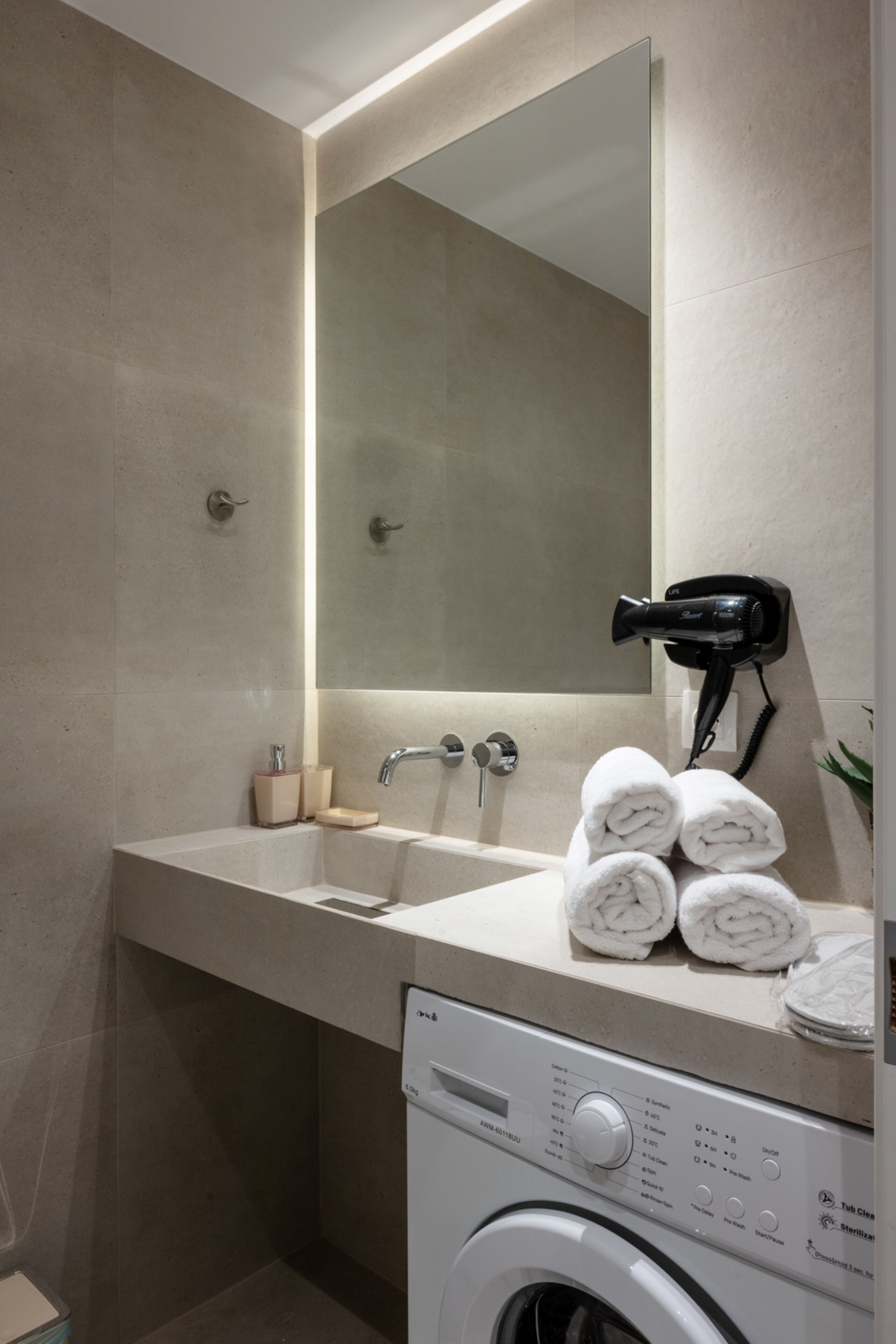 A modern bathroom with a large mirror, a sink, a hairdryer, and a washing machine.