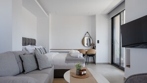 A modern hotel room with a sofa, a bed, a small table with candles, a mirror, and a TV. - Heart of Athens Apartments (Athens)