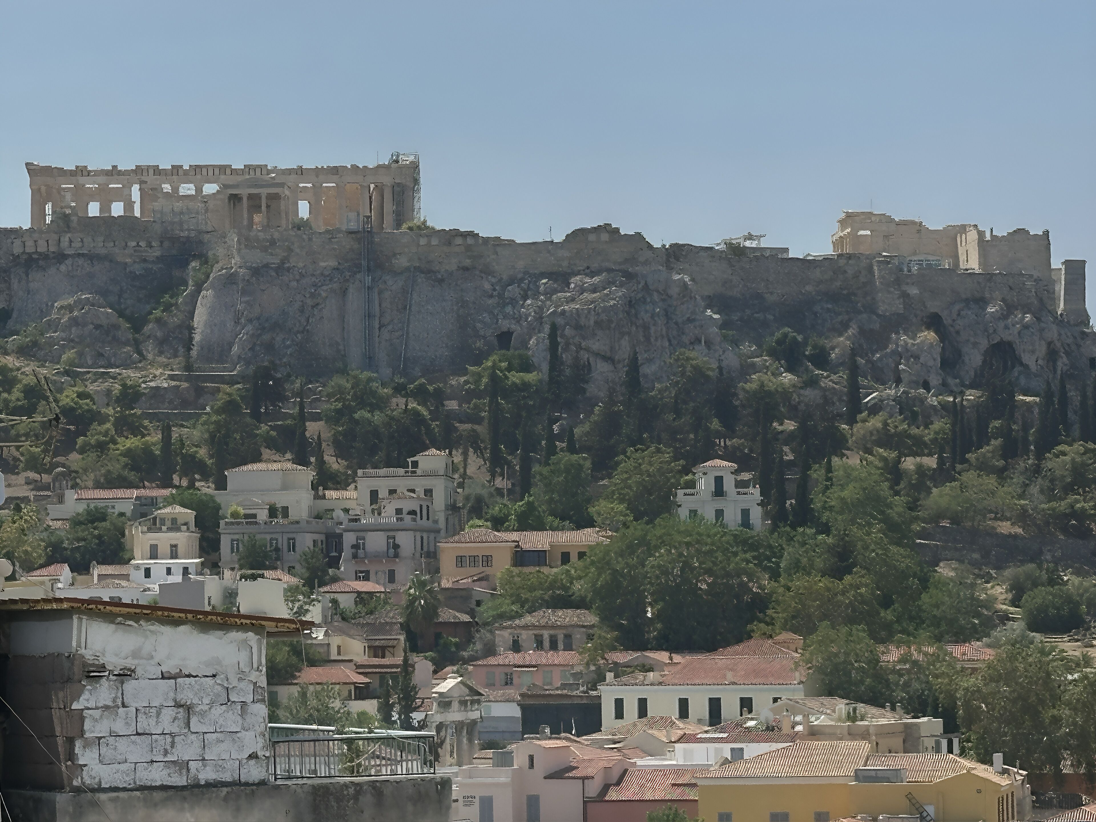 Une ville côtière avec des ruines historiques perchées sur une falaise, des immeubles d’habitation et une végétation luxuriante.