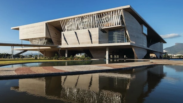 A modern building with a unique angular design, featuring a reflective water feature in front.