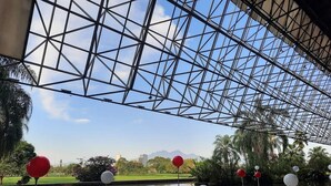 A glass ceiling structure with a view of a park and mountains in the background.