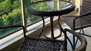A balcony with a glass table and wicker chairs, overlooking a lush green hillside.
