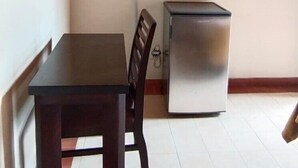 Una habitación pequeña con techo de madera, un televisor de pantalla plana en la pared, una mesa de madera oscura, una silla y un refrigerador pequeño.