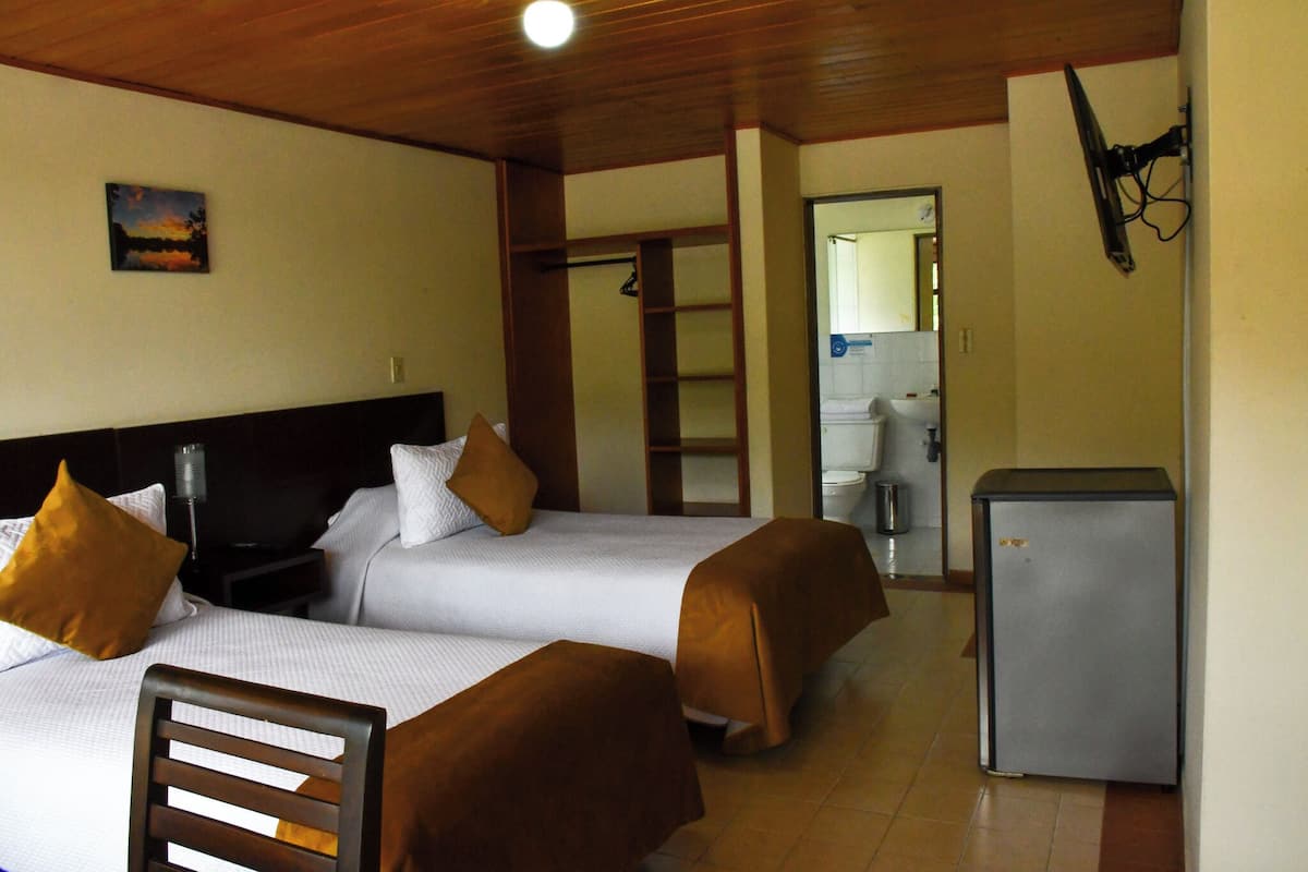 Quarto de hotel com duas camas, um pequeno frigorífico e um banheiro visível por uma porta aberta.