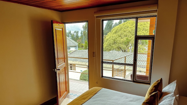 Un dormitorio con cama, almohadas, una ventana y una puerta abierta que da al exterior.