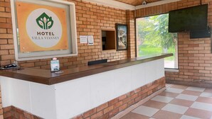 Zona de recepción de hotel con pared de ladrillo, mostrador de recepción, un cuadro enmarcado, televisor y ventana con vistas a zonas verdes.