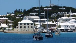 Uma marina com vários veleiros atracados, cercada por edifícios brancos e um horizonte com colinas.