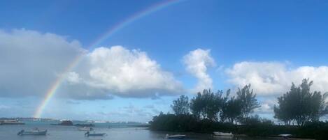 A river with boats, a rainbow, and trees in the background.