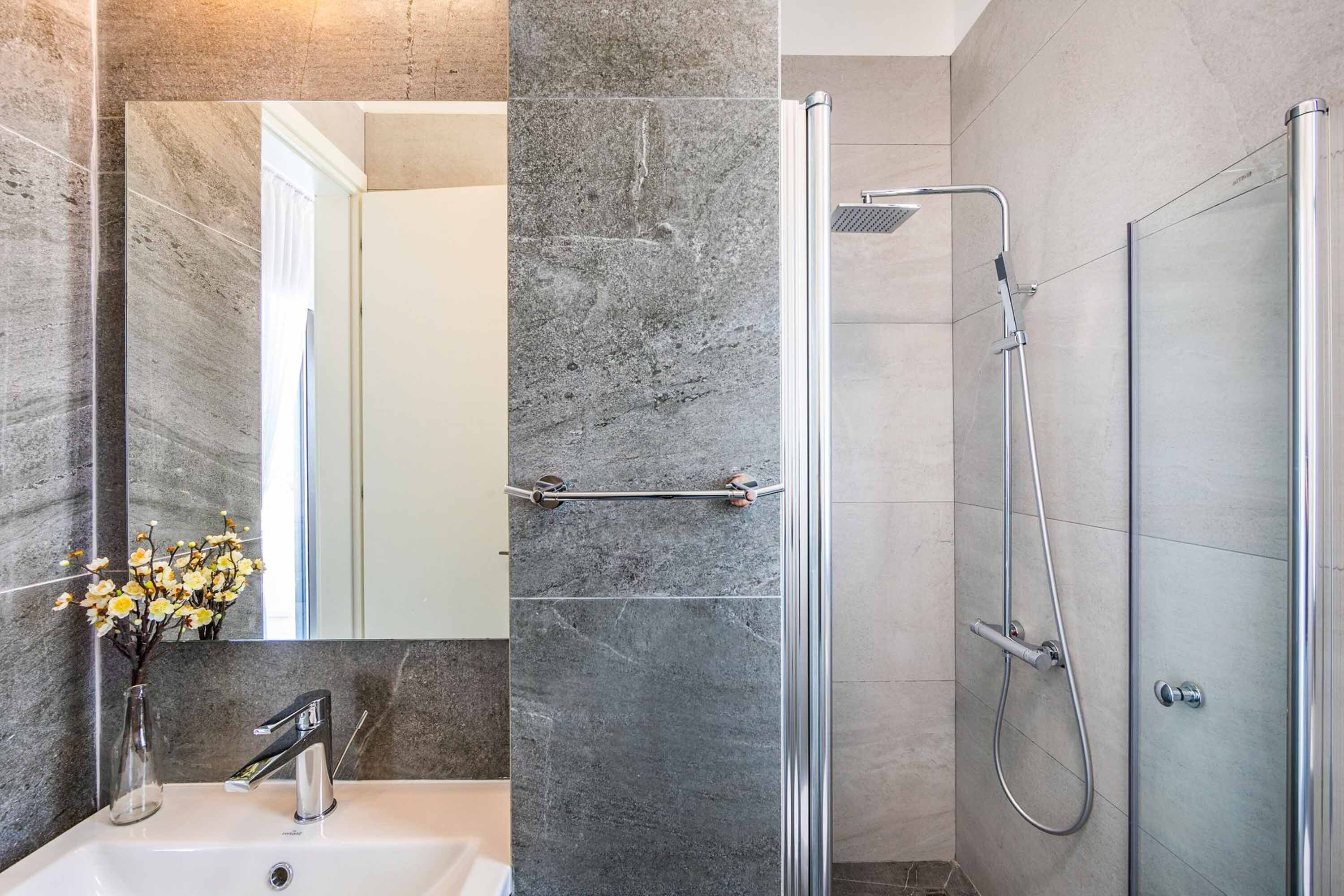 A modern bathroom with a glass-enclosed shower, a white sink, and a marble wall.
