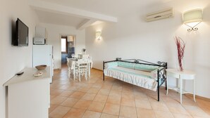 Une pièce spacieuse comprenant un lit, une table à manger et des chaises. On y trouve également un téléviseur fixé au mur, un réfrigérateur et un four à micro-ondes.