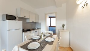 Une cuisine compacte avec des appareils électroménagers blancs, une table à manger pour quatre personnes et un petit meuble agrémenté d’un vase.