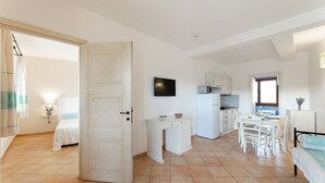 Une pièce compacte et bien éclairée, comprenant un lit, une petite kitchenette et un coin repas.