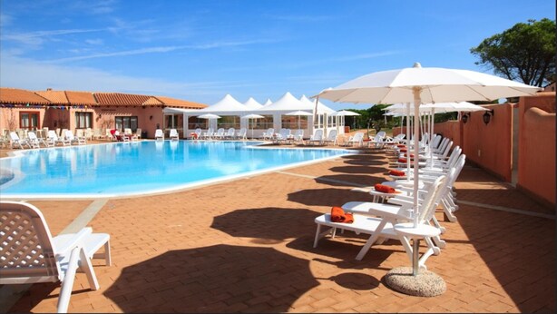 Une piscine entourée de bâtiments aux toits recouverts de tuiles rouges, avec des chaises longues blanches et des parasols.