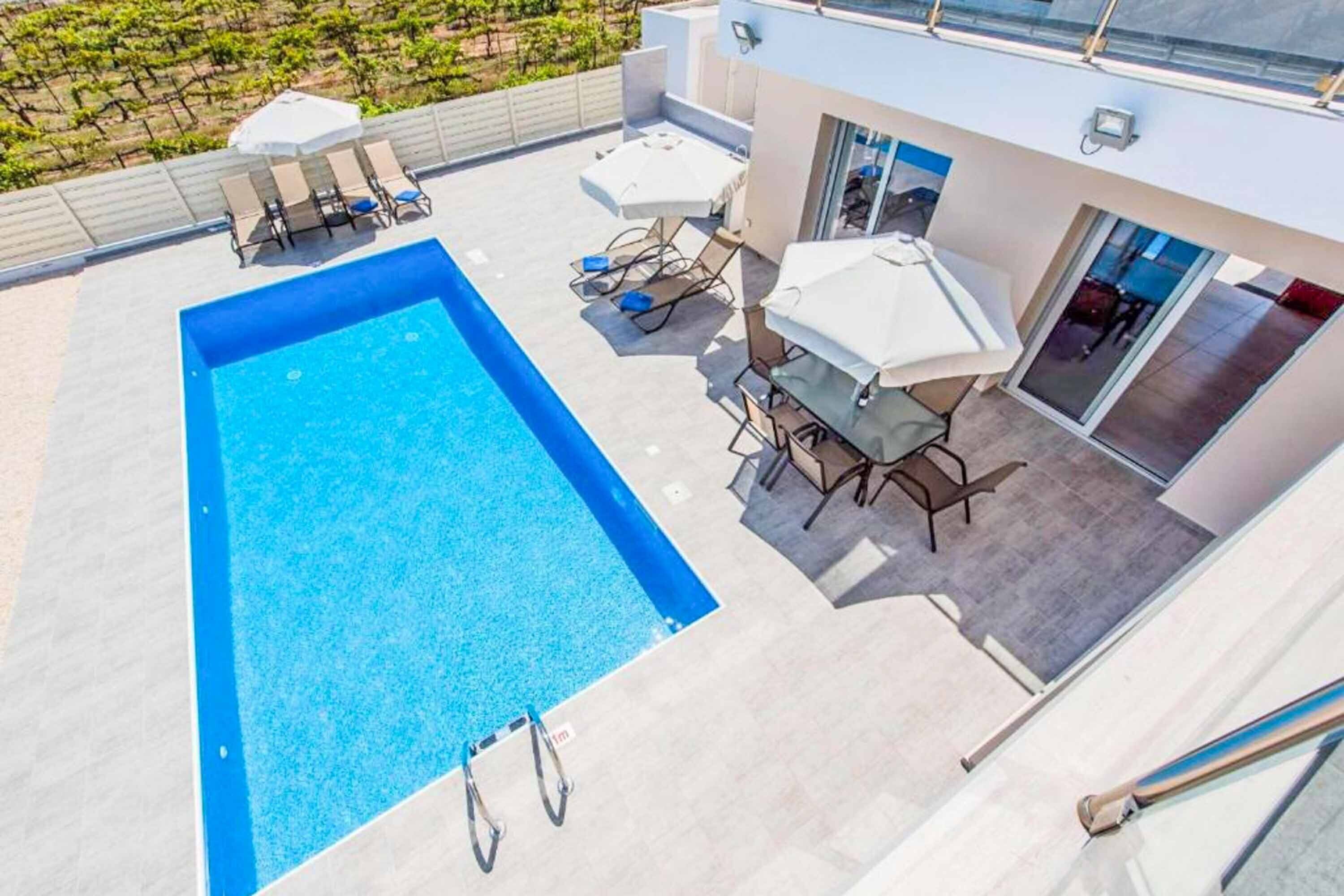 A rooftop pool with a clear blue pool, lounge chairs, and a table with umbrellas.