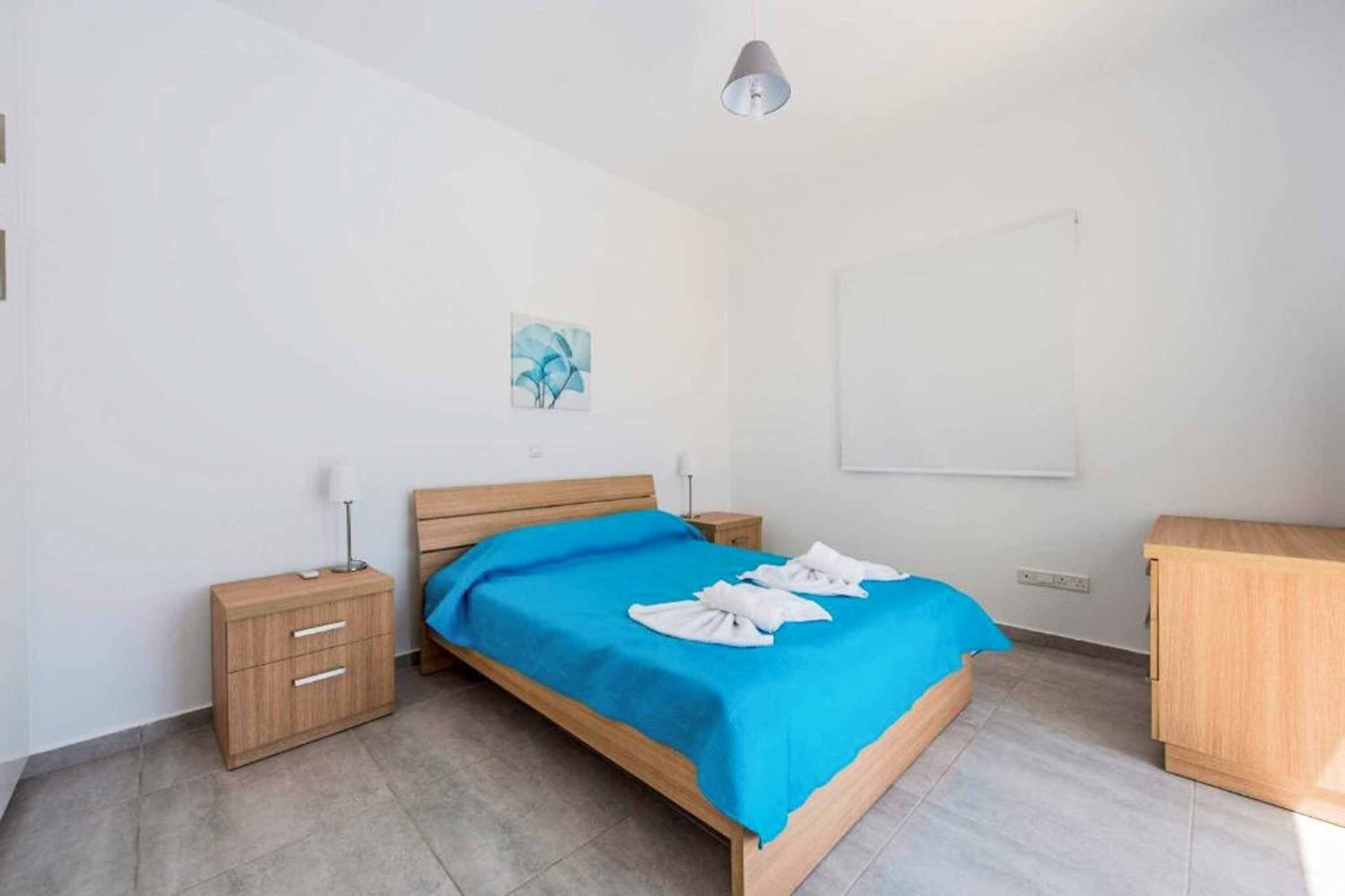 A bedroom with a bed, a nightstand, a wooden dresser, and a wall-mounted light fixture.