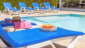 Un espace aménagé au bord de la piscine, avec des chaises longues bleues et un panier de pommes.