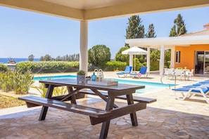 A covered outdoor area with a pool, lounge chairs, and a picnic table. - Villa Theo - Four Bedroom Villa, Sleeps 8 (Peyia)
