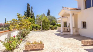 Une cour avec un bâtiment blanc, un espace de repos abrité et une variété de plantes.