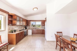 A modern kitchen with wooden cabinets, a dining table, and chairs. - Villa Theo - Four Bedroom Villa, Sleeps 8 (Peyia)