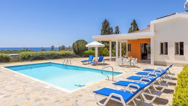 A swimming pool with lounge chairs, a covered seating area, and a view of the sea. - Villa Theo - Four Bedroom Villa, Sleeps 8 (Peyia)