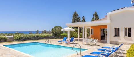 A swimming pool with lounge chairs, a covered seating area, and a view of the sea.