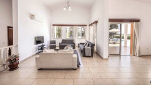 A spacious living room with a large sofa, a TV, and a balcony with outdoor furniture. - Villa Theo - Four Bedroom Villa, Sleeps 8 (Peyia)