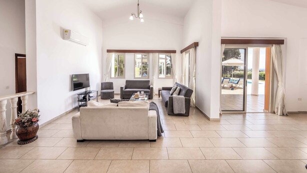 Un salon spacieux avec un grand canapé, un téléviseur et un balcon aménagé avec du mobilier d’extérieur.