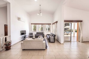A spacious living room with a large sofa, a TV, and a balcony with outdoor furniture. - Villa Theo - Four Bedroom Villa, Sleeps 8 (Peyia)