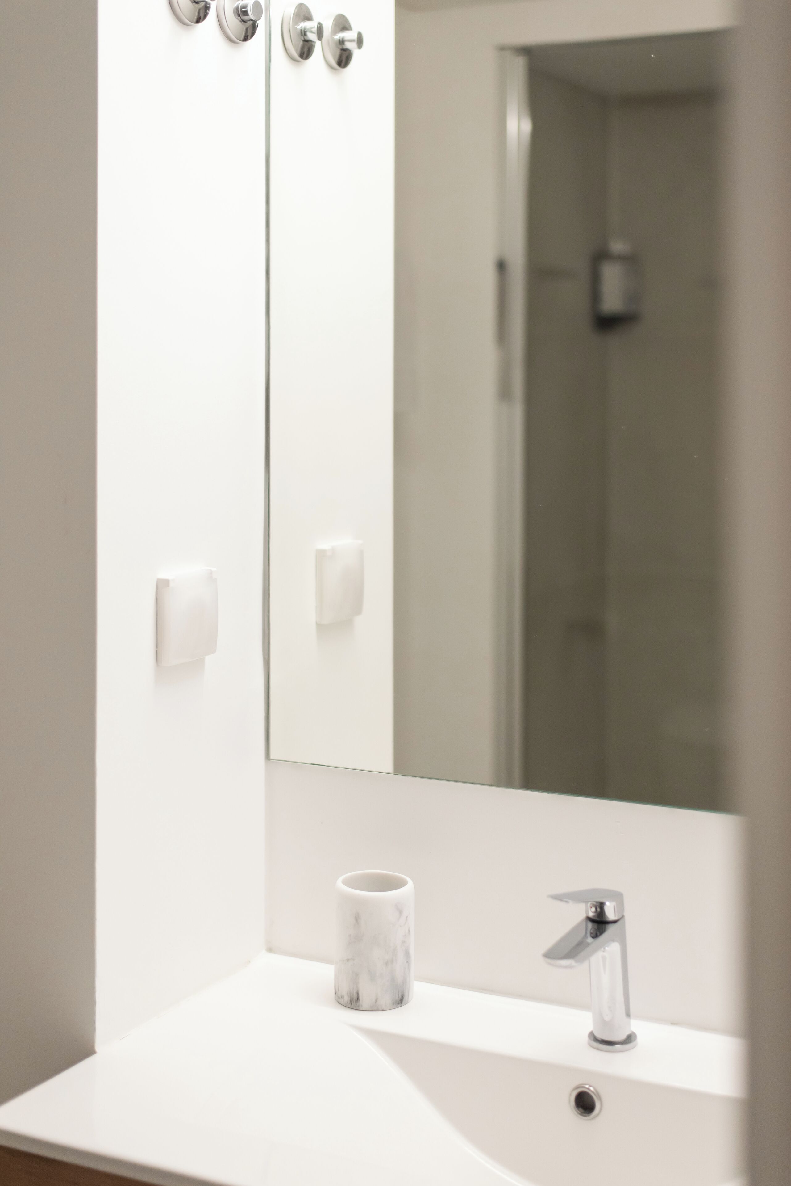 Un baño moderno con un lavabo blanco, una taza de mármol y un espejo grande que refleja una zona de ducha.