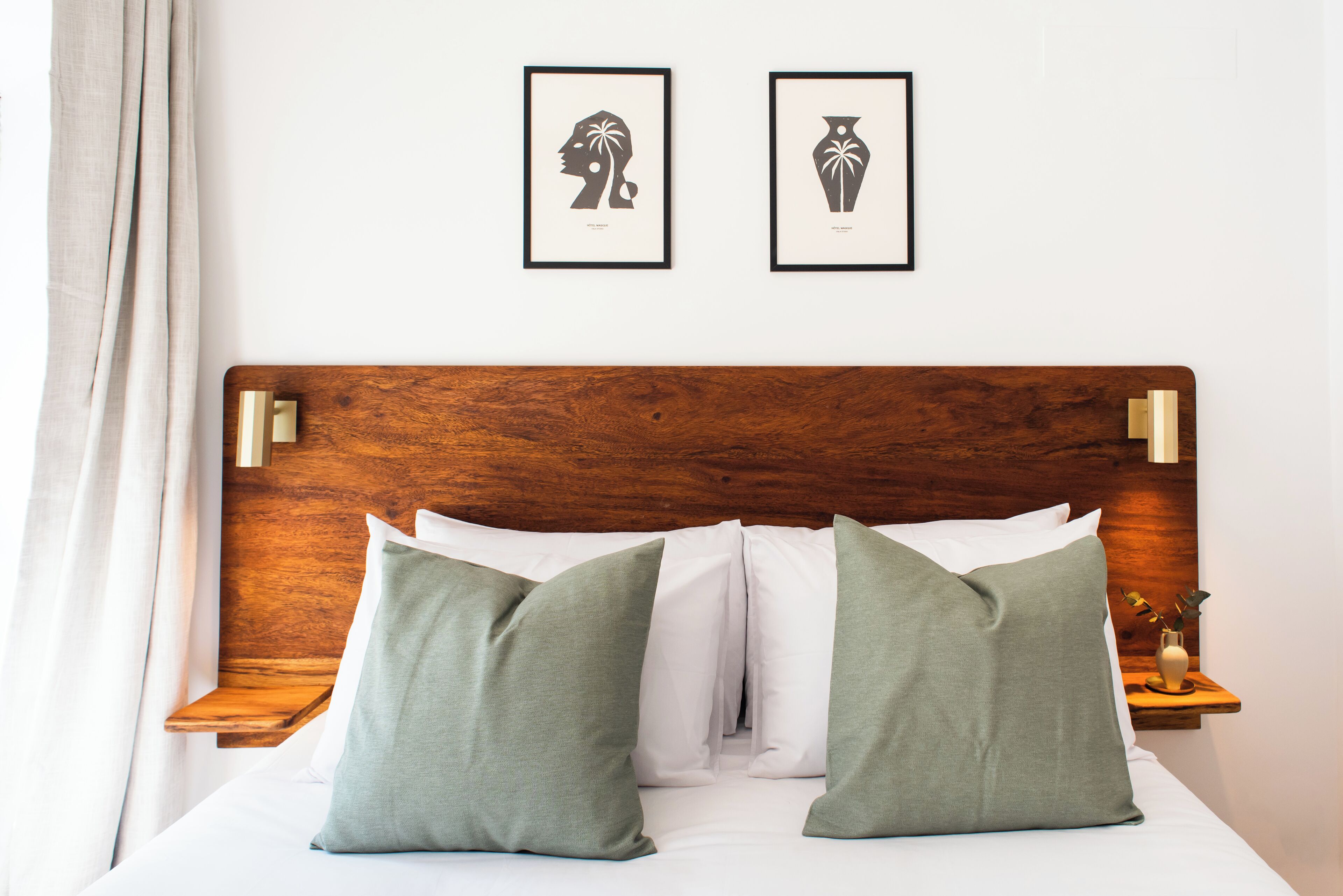 Una cama bien hecha con cabecera de madera, dos almohadas verdes y dos cuadros enmarcados en la pared de arriba.