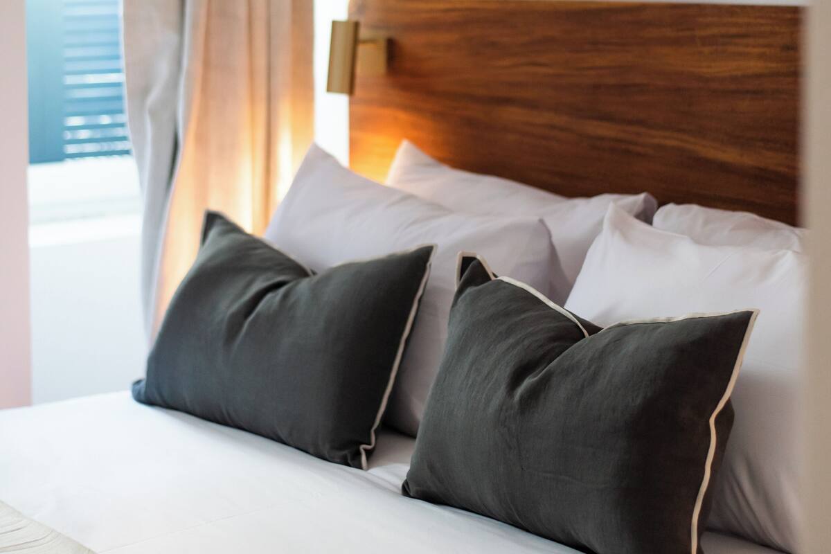 Une chambre d’hôtel avec une tête de lit en bois, une grande fenêtre offrant une belle vue et deux œuvres d’art encadrées accrochées au mur.