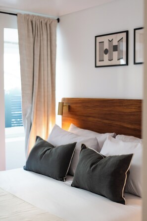 Une chambre d’hôtel avec une tête de lit en bois, une grande fenêtre offrant une belle vue et deux œuvres d’art encadrées accrochées au mur.