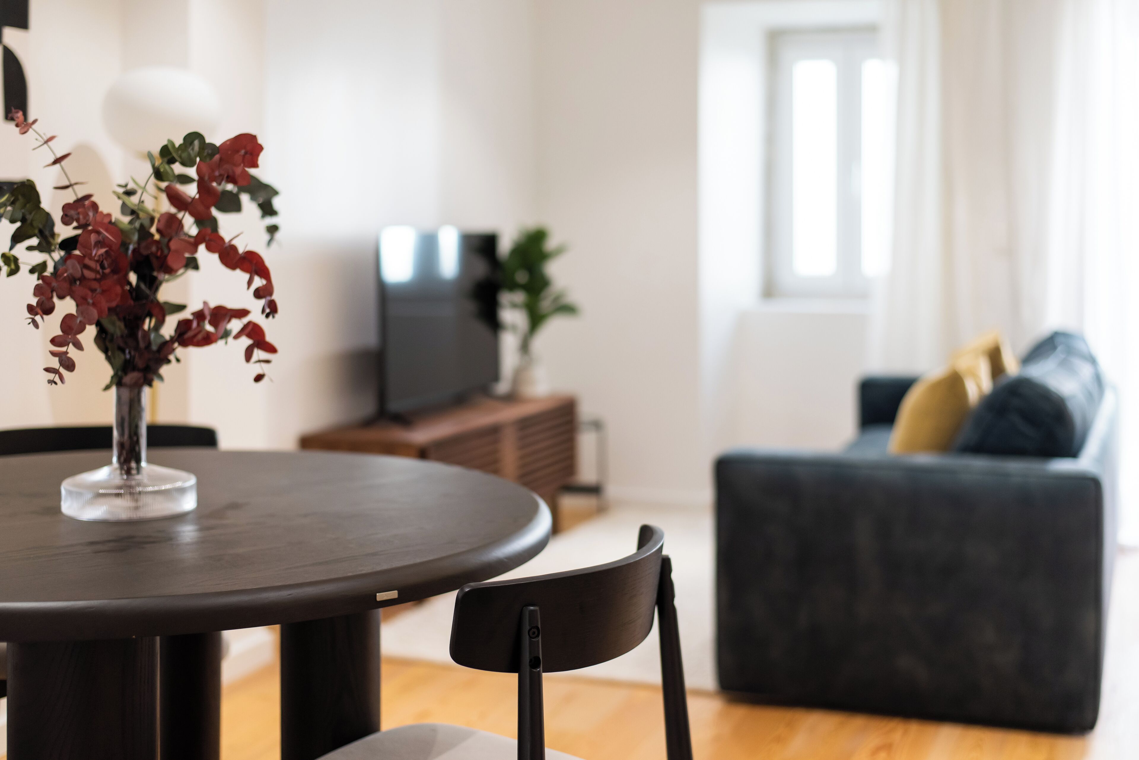Una mesa de comedor con un florero, un sofá oscuro y un televisor en una sala de estar.