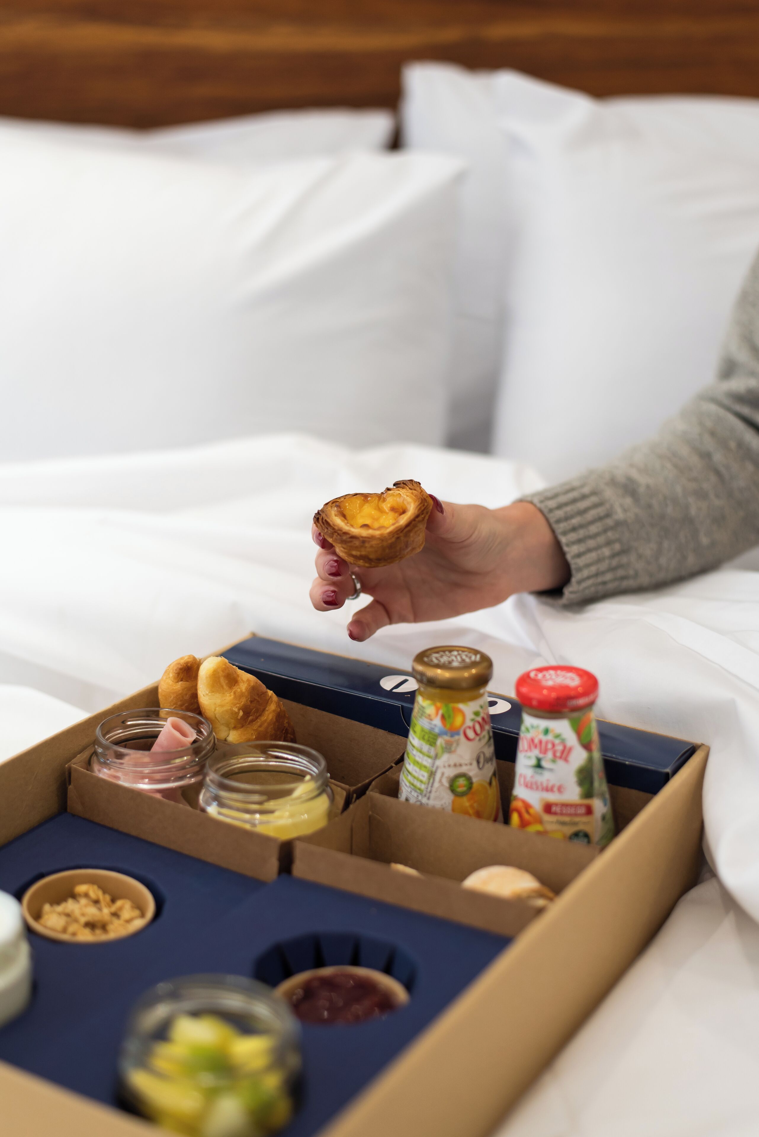 Una caja de desayuno con pasteles, mermeladas y salsas sobre una cama.