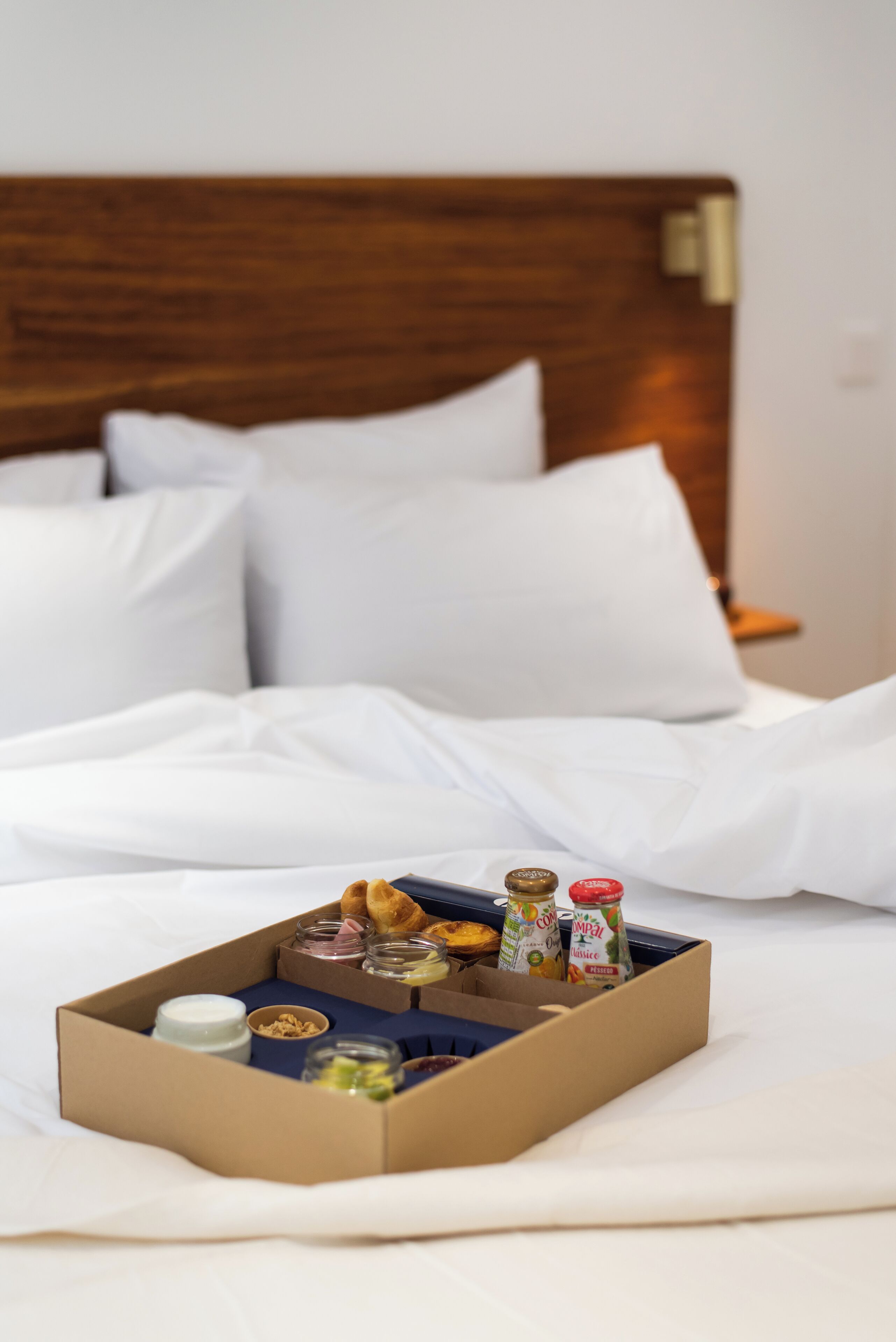 A neatly made bed with white linens and a breakfast tray containing croissants, yogurt, and jam.