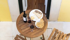 A wooden table with a bottle of wine, glasses, and a plate of cheese and crackers. Two wooden chairs are placed around the table. - The Haus - Alegria (Lisbon)