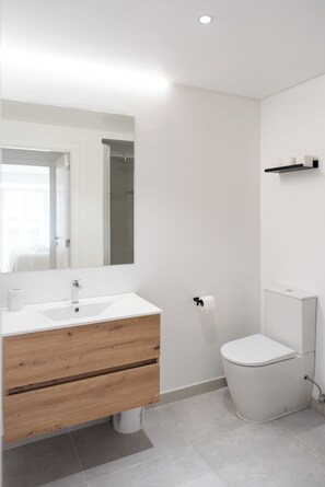 Une salle de bain moderne avec un lavabo blanc, un meuble-lavabo en bois, un grand miroir, des toilettes et un espace douche.