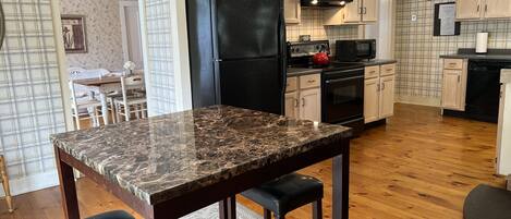 Una cocina con encimera de mármol, armarios de madera, refrigerador negro, microondas y estufa.